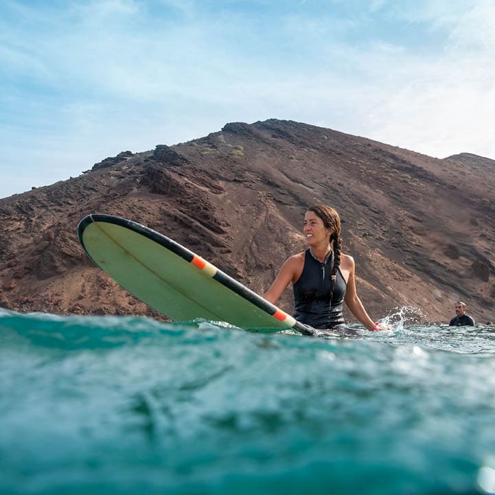 Beautiful young brunette woman surfing in Fuerteventura in the Atlantic ocean on the background of blue sky, clouds and transparent waves