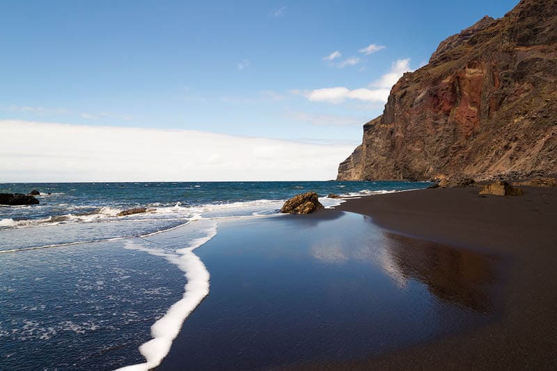 A black sand beach at the atlantic ocean at La Gomera, one of the canary islands. The sky is morrored in the wet sand.