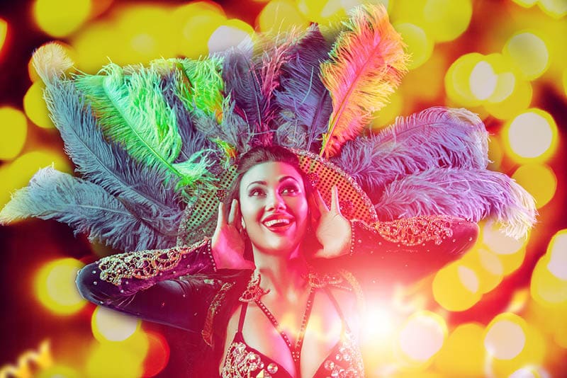Beautiful young woman in carnival peacock costume. Beauty model woman at party over holiday background with magic glow. Christmas and New Year celebration. Glamour lady with perfect make up and hairstyle. Image is not body shape retouched