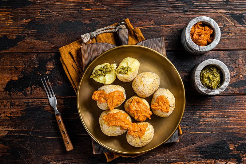 Canary Islands dish Papas Arrugadas wrinkly salty potatoes with and Mojo picon red spicy sauce. Wooden background. Top view.